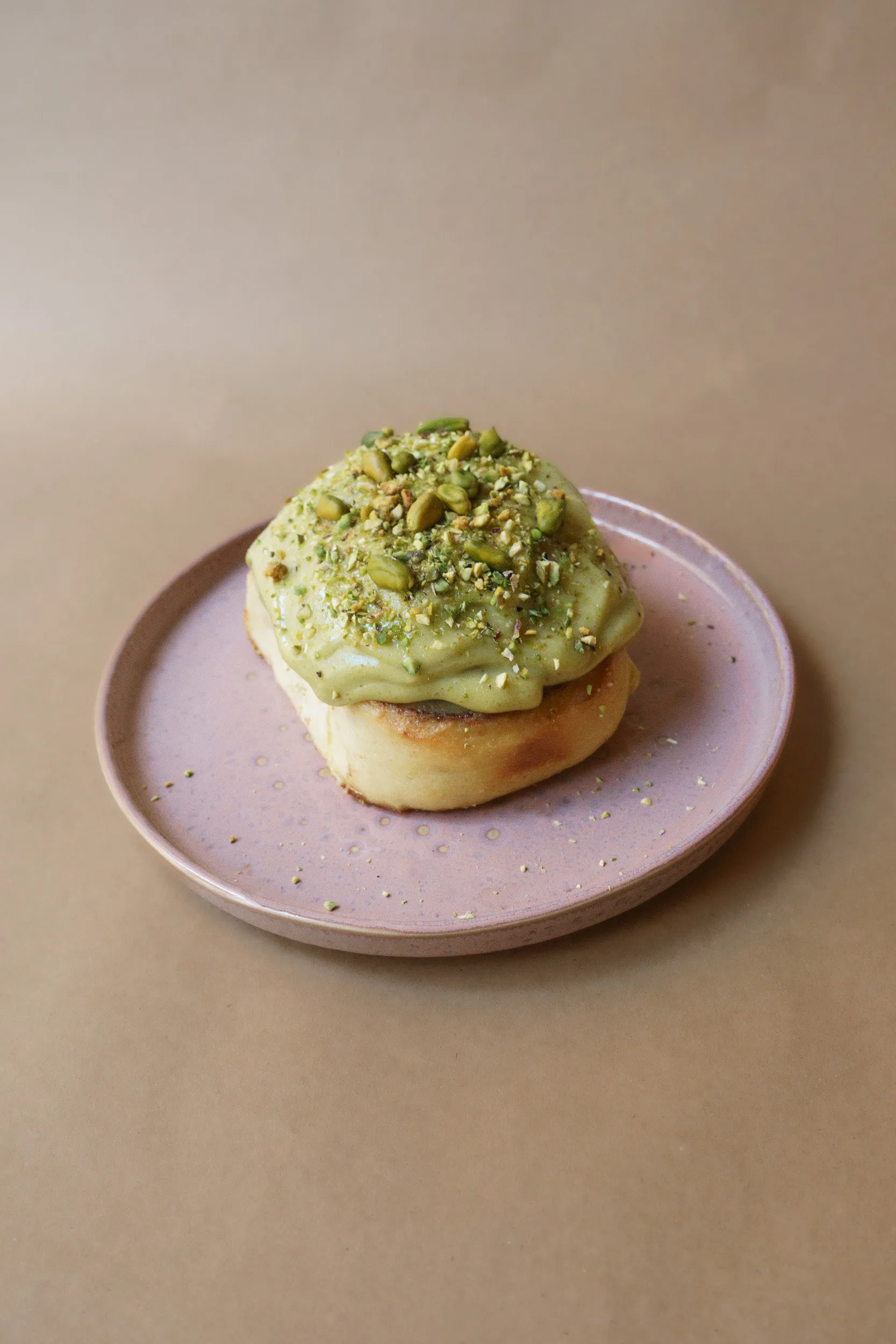 Pistachio cinnamon roll with pistachio cream and crushed nuts, on a pink plate